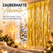 Goldener Lamettavorhang am Fenster, festlich dekoriert mit Sternlampe, Kerzen, Tannenzweigen und Kugeln.