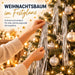 Hände schmücken einen leuchtenden Weihnachtsbaum mit silbernen Girlanden, Kugeln und Schneeflocken-Anhänger